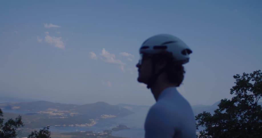 Slow motion shot of a cyclist in a helmet enjoying the breathtaking view of the sea and mountains from a high vantage point at dusk