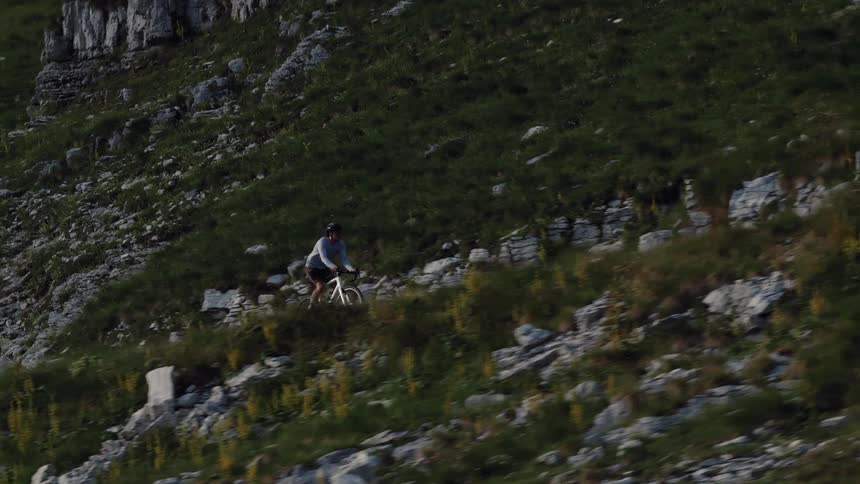 Wide shot of a male cyclist riding his bike along a steep and rocky mountain trail