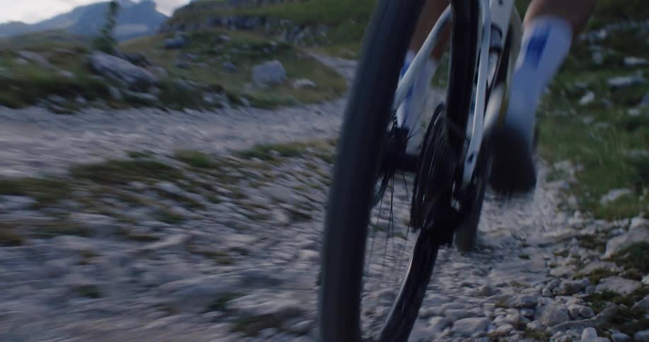 Dynamic close-up of a cyclist pedaling up a rugged gravel path on a mountain in slow motion