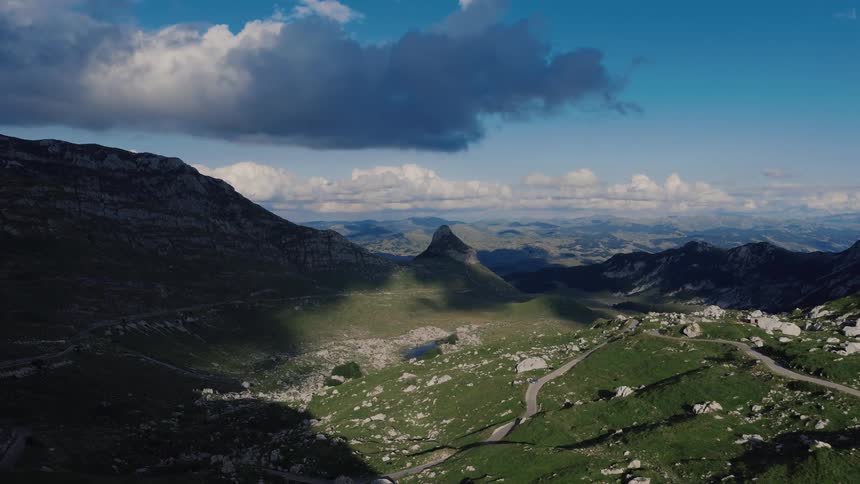 A stunning aerial view of a majestic mountain valley with a winding road, under a dramatic cloudy blue sky