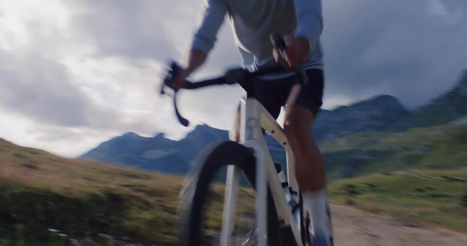 A professional cyclist rides past the camera on a gravel bike through a rugged mountain pass