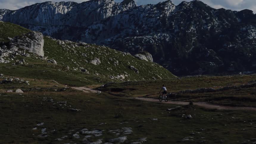 A cyclist pedals along a remote dirt path through a dramatic and expansive mountain valley