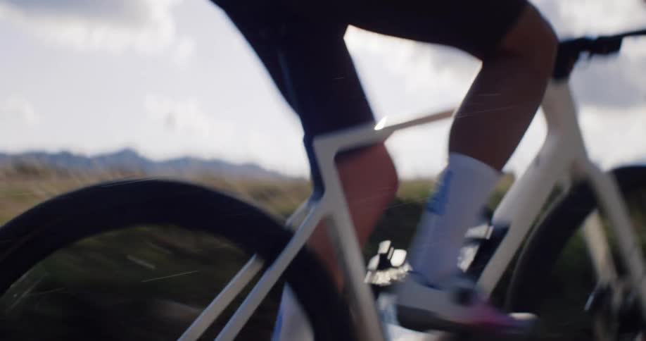 A cyclist pedals in slow motion along a rugged mountain gravel path, with close-up shots of the wheels and gears turning against the sun