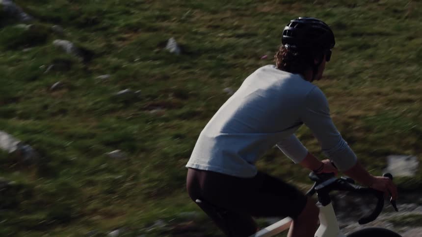 Slow motion side-view tracking shot of a man cycling uphill on a scenic mountain road