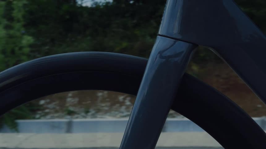 A close-up shot of a modern road bike's front wheel and fork as it spins along a paved path