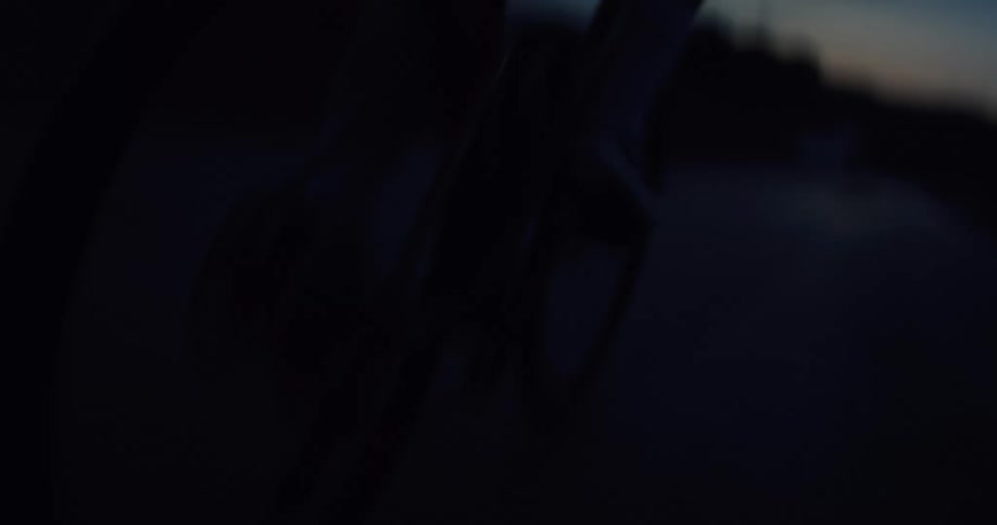 A low angle close-up captures the silhouette of a cyclist riding their bicycle on a dark road at dusk