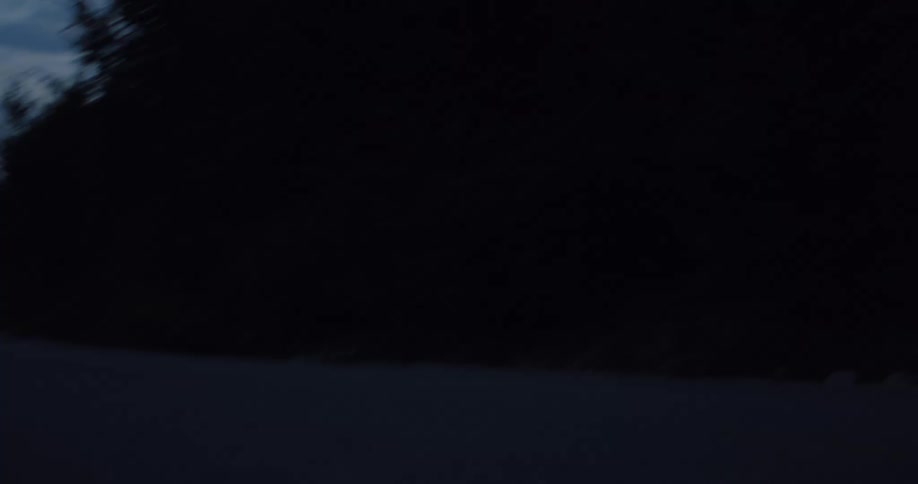Low angle of a silhouetted cyclist speeding down a dark, empty road at twilight