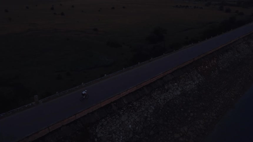 Aerial view of a solitary cyclist riding along a road on top of a dam during twilight