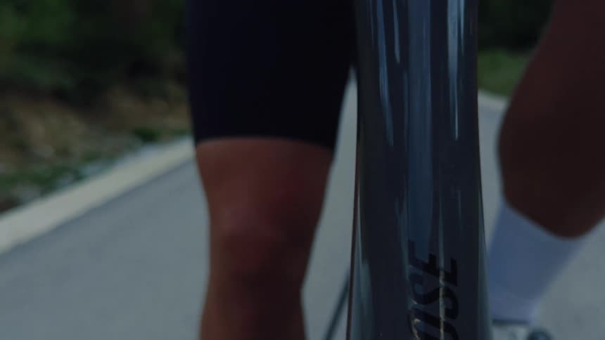 Close-up on the muscular legs of a professional cyclist pedaling a road bike along a country lane