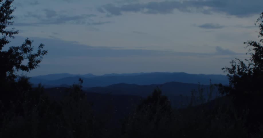 A blurry figure speeds past a layered mountain range at dusk, creating a motion blur effect