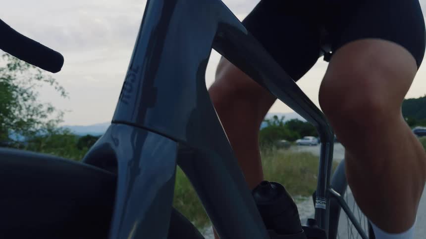 Slow-motion close-up of a professional cyclist pedaling a sleek road bike along a country road, ending with a POV shot