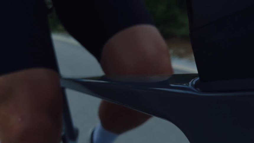 A dramatic slow-motion close-up captures the powerful leg muscles of a cyclist pedaling on a sleek road bike