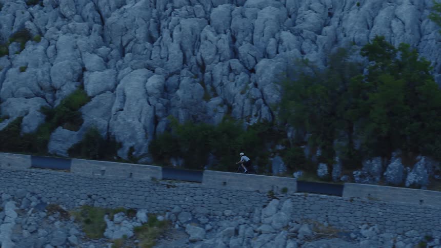 A determined cyclist pedals uphill on a winding road carved into a steep, rocky mountainside
