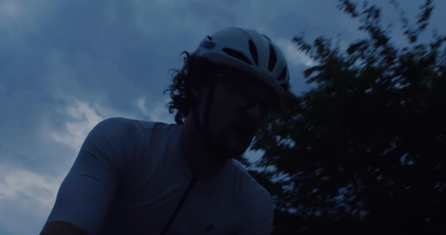 A focused male cyclist in a helmet pushes through a challenging ride during the dark blue twilight hours