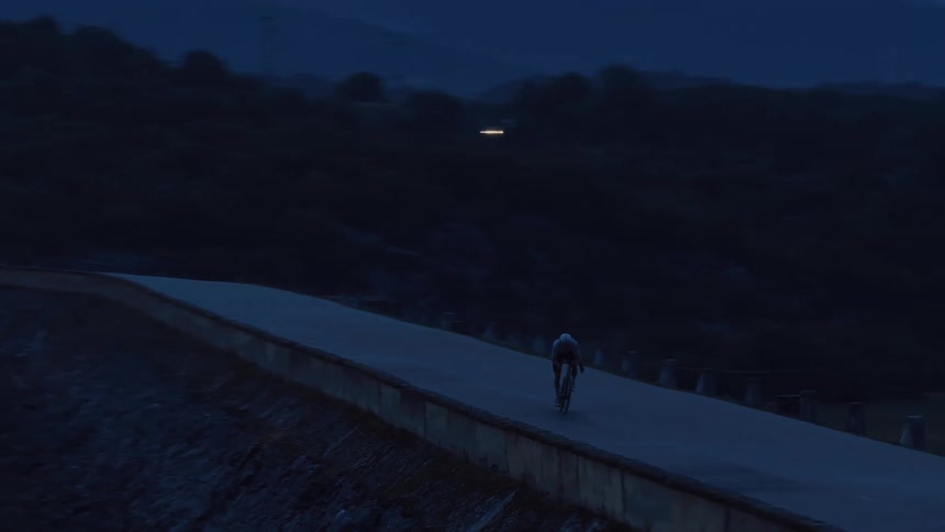A lone cyclist rides along the top of a remote dam road in the predawn darkness