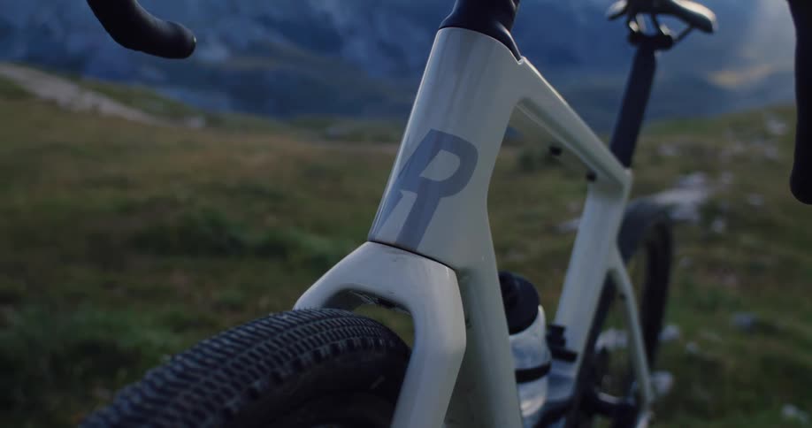 A detailed slow-motion close-up of a modern gravel bicycle frame against a scenic mountain backdrop