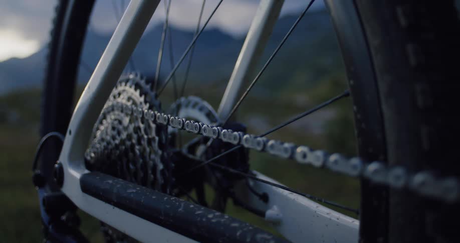 A slow-motion close-up of a mountain bike's rear cassette and chain with a rugged mountain landscape in the background