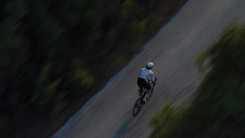 Aerial top-down view of a cyclist in professional gear riding down a secluded road surrounded by a dense forest