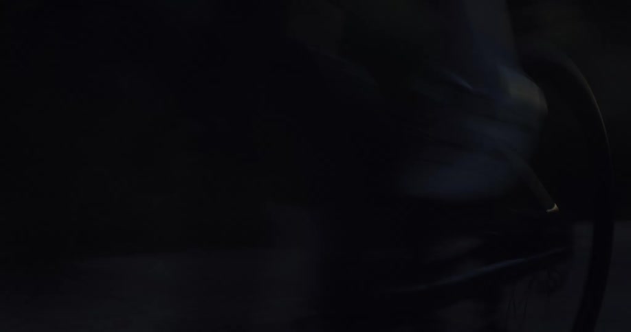 Close up of a cyclist wearing a helmet as they speed past the camera on a dark road at sunset