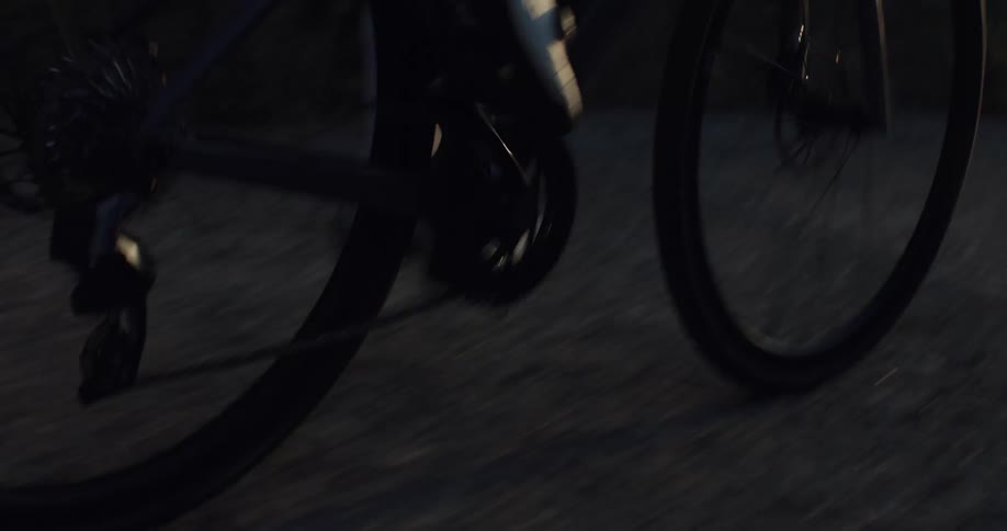 Dynamic close-up of a road bike's wheels and a cyclist's feet pedaling quickly on a paved road at golden hour