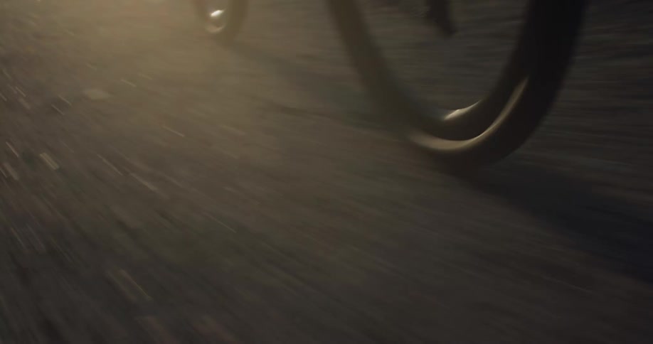 A dramatic low-angle close-up of a bicycle's wheel and pedals in motion on a paved road at night