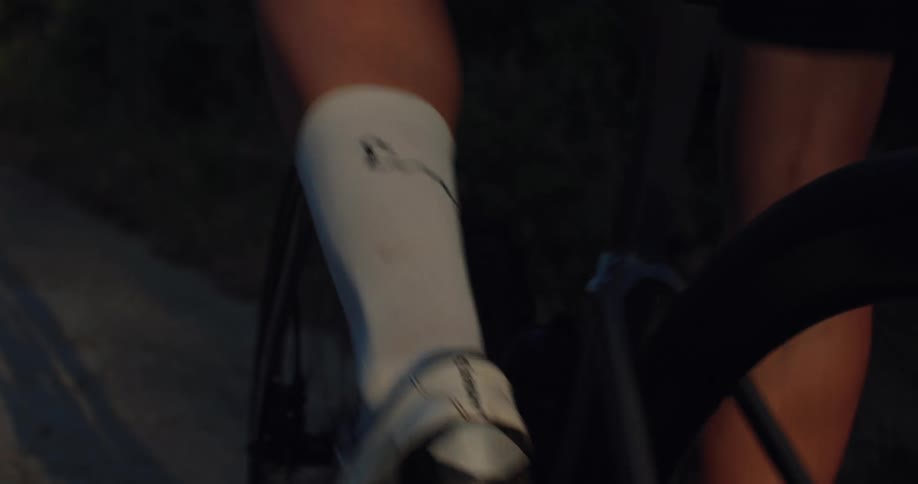 Detail shot in slow motion of a professional cyclist's legs turning the pedals at twilight