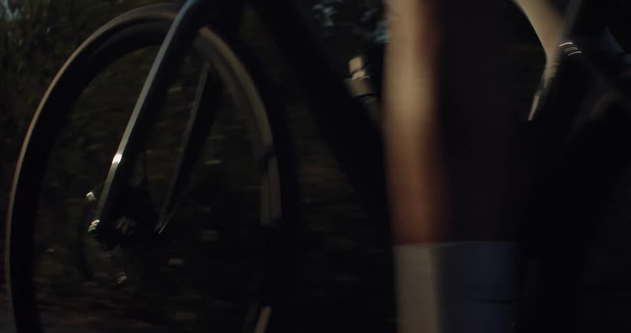 Dynamic close-up of a road bike's spinning wheels and pedals as a cyclist rides through a park during sunset