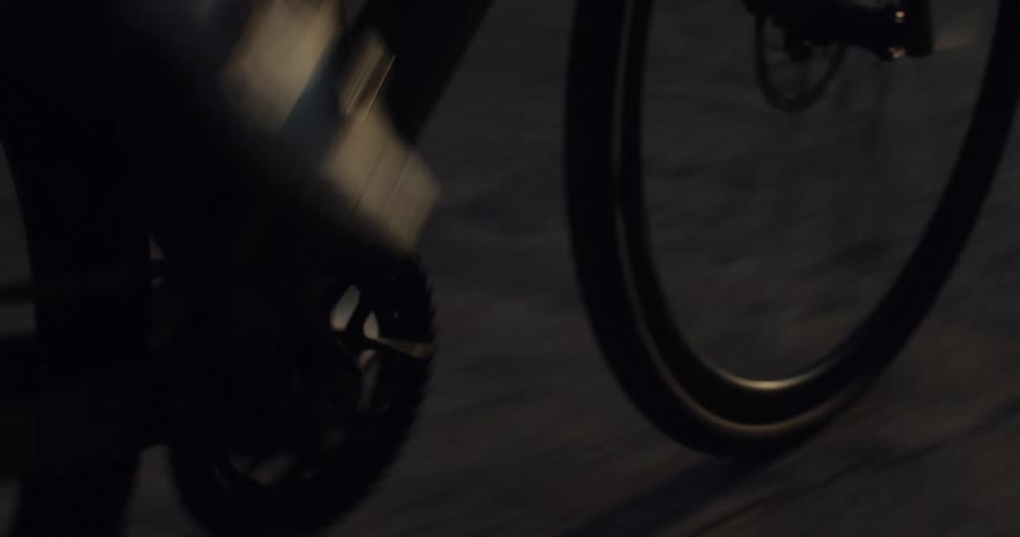 A close-up view shows a cyclist's feet pedaling on a road bike during the golden hour