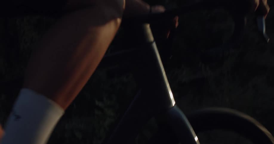 A professional cyclist's legs and hands are seen in a slow-motion close-up as they ride into the sunset