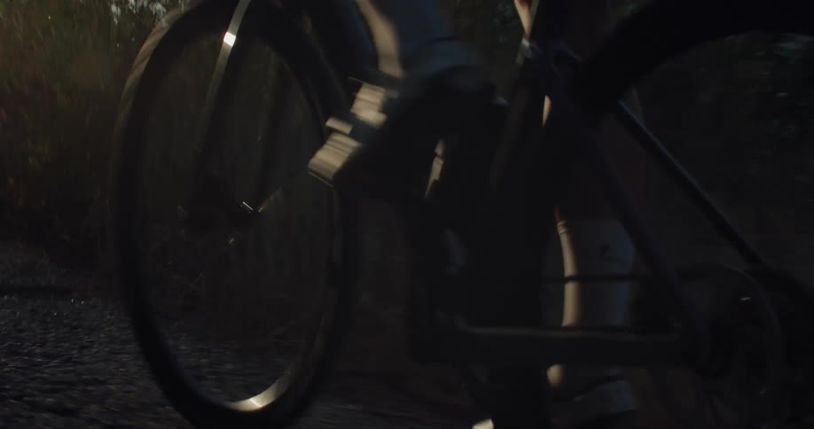 Dynamic low-angle close-up of a cyclist pedaling on a rural road as the sun flares in the background