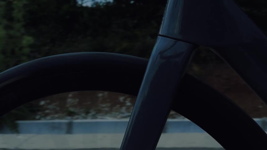 A close-up of a modern bicycle's front wheel and fork spinning smoothly along a road at dusk