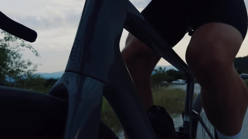 A dynamic first-person perspective of a cyclist pedaling a modern road bike along a country road at dusk