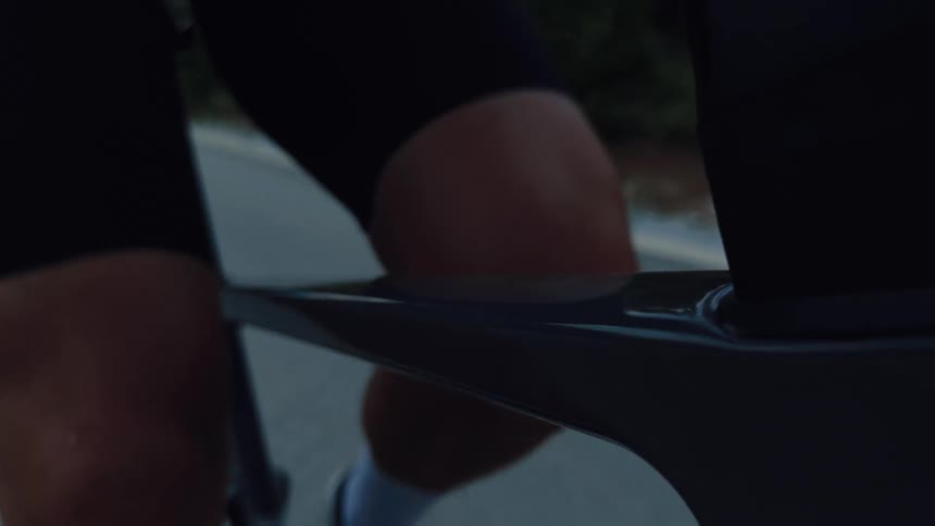 Close-up slow-motion shot of a cyclist's muscular legs pedaling a road bike at dusk