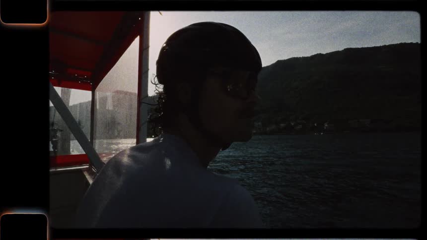 A man wearing a helmet enjoys a peaceful boat ride across a lake in this authentic Super 8mm film footage