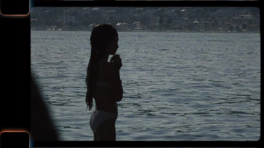 Vintage home movie captures the silhouette of a young girl standing in the ocean on a summer day