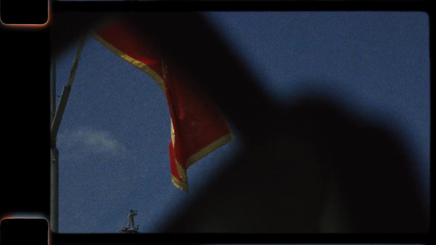 A vintage film-style shot of the Montenegrin flag waving in the wind against a blue sky and green hills