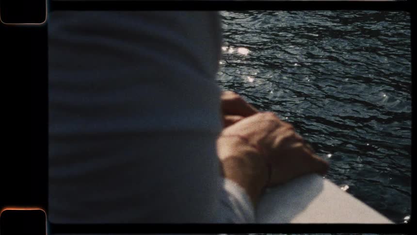 A vintage, over-the-shoulder shot of a person's hands resting on the railing of a boat as it moves through sun-dappled water