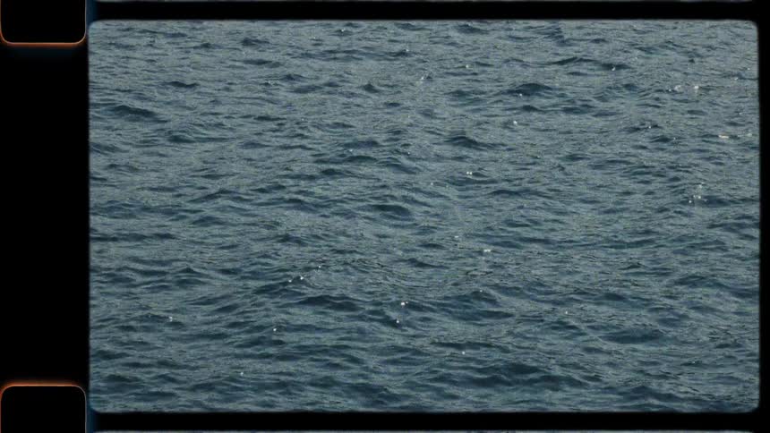 A vintage film-style shot captures the gentle movement of open ocean waves under the sun