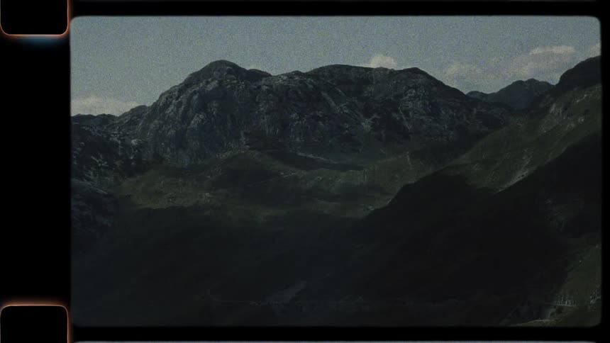 An authentic Super 8 film captures a static view of a majestic and shadowy mountain landscape