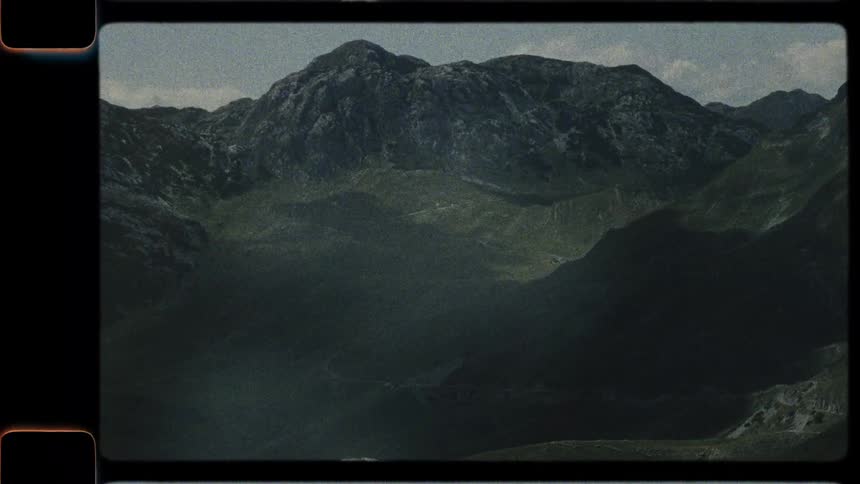 A grainy, vintage-style pan shot reveals a majestic green and rocky mountain landscape