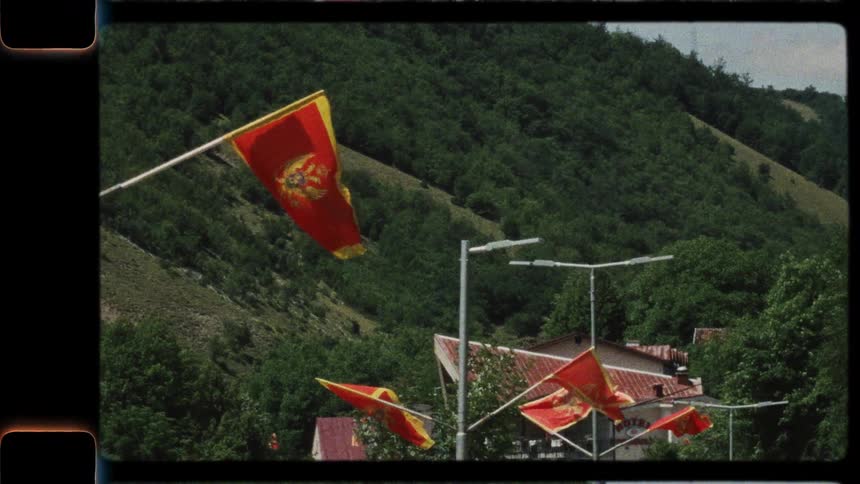 Vintage-style footage shows Montenegro flags waving in slow motion against a lush green mountain backdrop