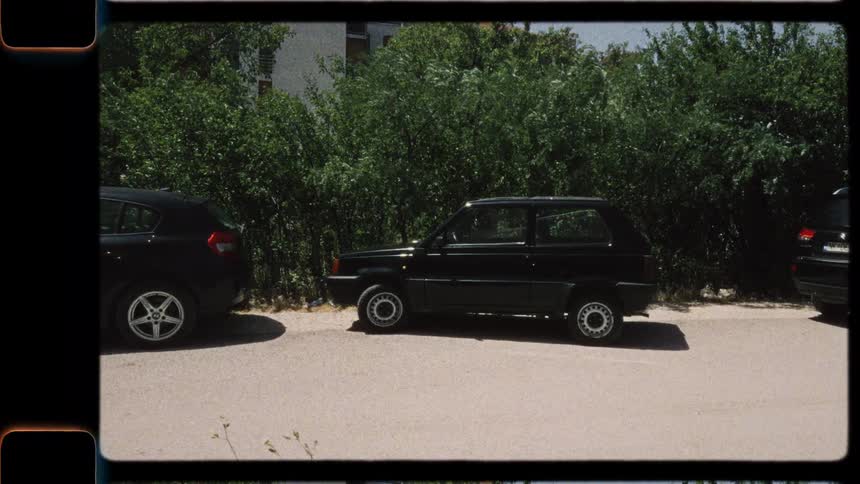 A profile shot of a classic black Fiat Panda parked on the street, with a vintage Super 8 film aesthetic