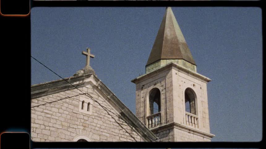 Vintage footage of an old stone church with a bell tower and clock, shot on a sunny day