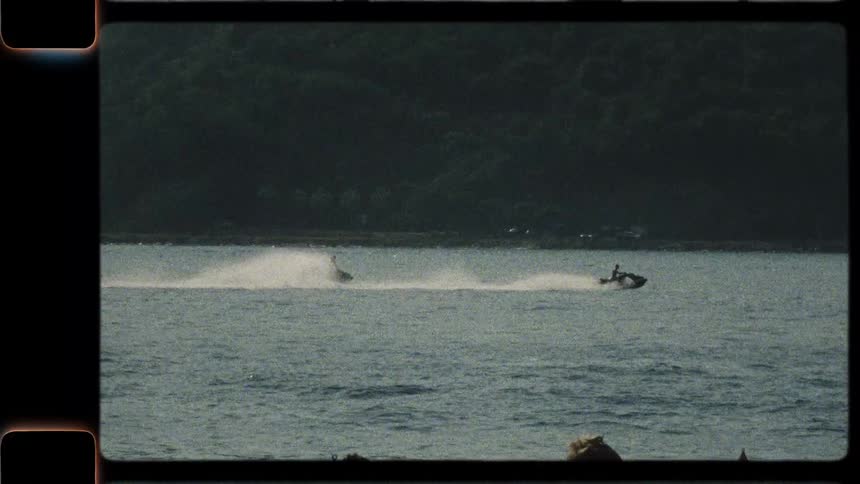 Vintage Super 8mm film of two people riding jet skis across a lake on a sunny summer day