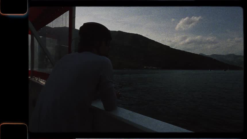 A man wearing a hat gazes out from the deck of a moving boat at a vast mountain lake in this authentic vintage footage