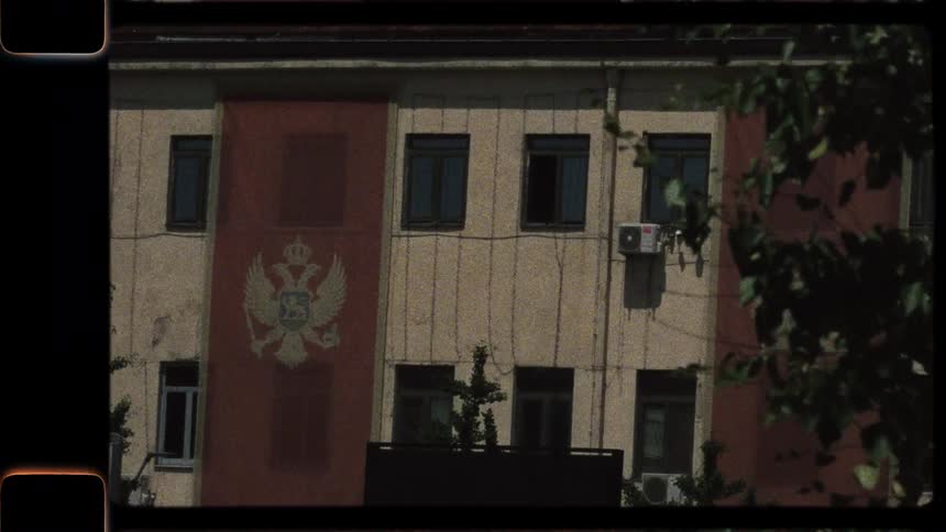 Vintage 8mm film style footage of a building with the Montenegrin coat of arms on a large red banner