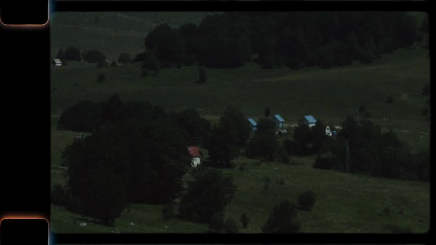 A vintage Super 8mm film captures a scenic drive through a lush, green mountain valley with a small village nestled among the trees