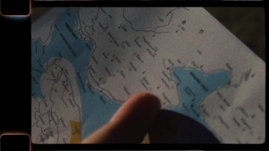 A vintage Super 8 film shows a close-up of a person's finger planning a journey on a map of coastal Montenegro