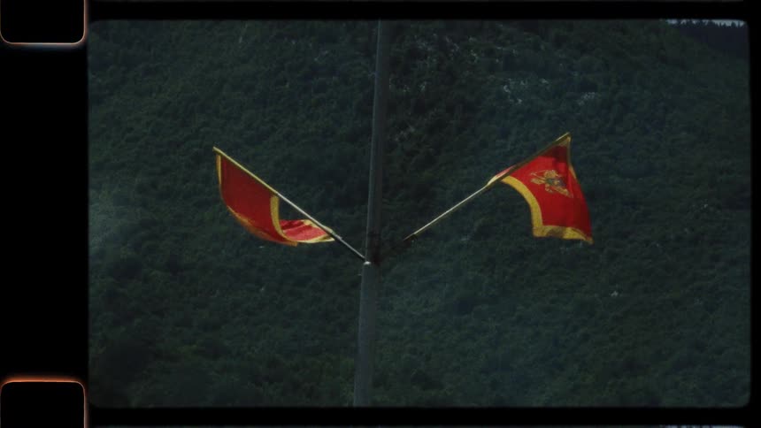 Two Montenegrin flags wave slowly against a green mountain backdrop, captured on vintage film
