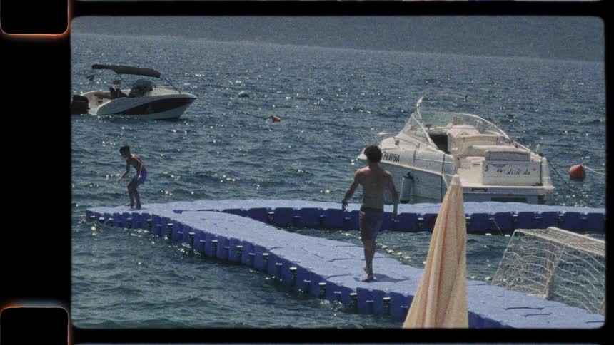 Vintage 8mm footage captures a man diving into the sea from a floating pier after playing with a boy on a sunny day